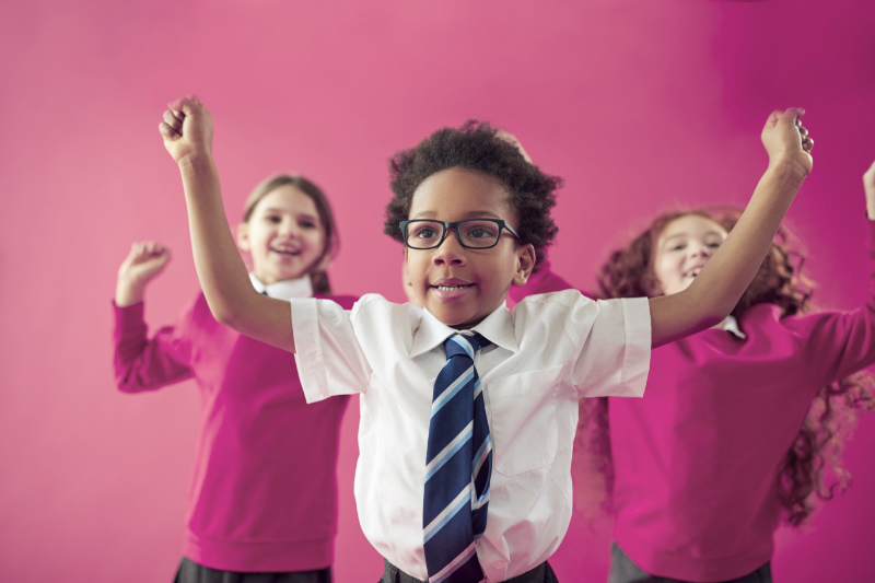 Group Of Excited Early Years School Pupils Wearing Uniform Having Fun Against pink Studio Background
